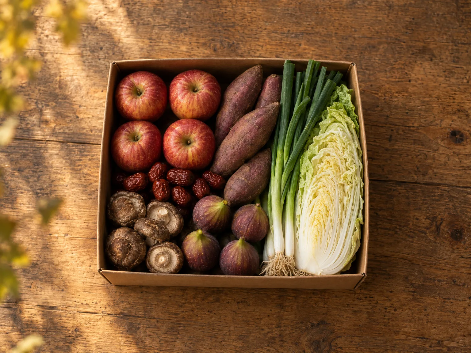 위에서 내려다본 작은 상자. 사과 네 알과 고구마, 대추, 표고, 쪽파 반 단, 배추 반 통, 무화과가 담겨 있다